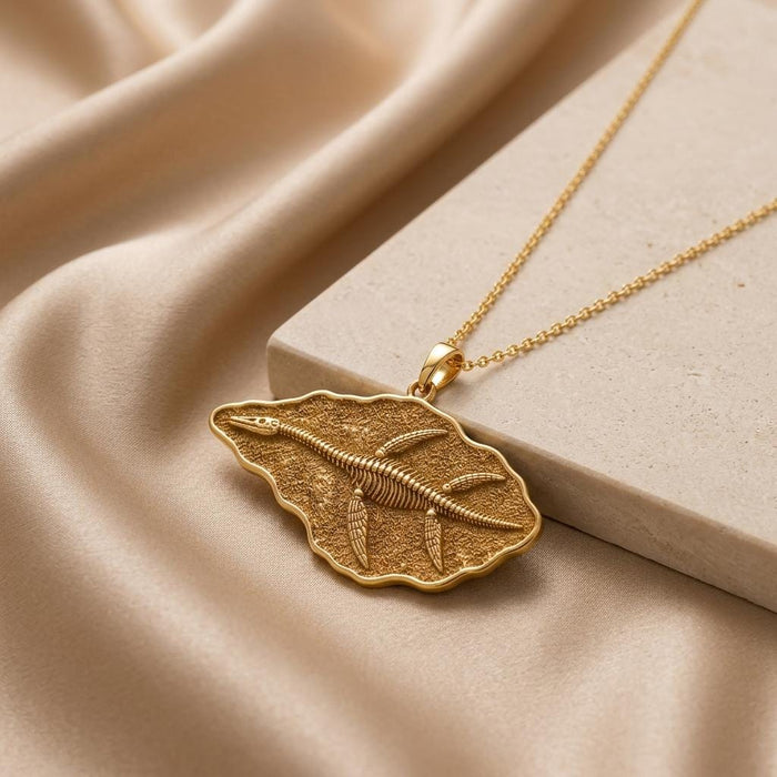 Gold Plated Silver Elasmosaurus Fossil Pendant on champagne satin beside a stone block