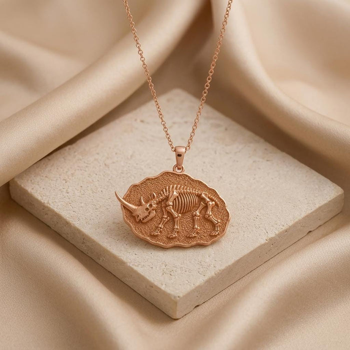 Rose Gold Plated Elasmotherium Fossil Pendant displayed on a pale stone block with satin fabric