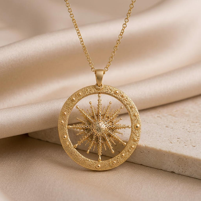 Gold-finish Elnath Star Pendant Necklace with a dimensional starburst inside a textured circular frame on folded champagne satin