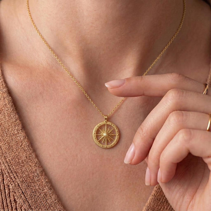 Close view of the gold-finish Elnath Star Pendant Necklace worn at the neckline, showing the textured circular frame