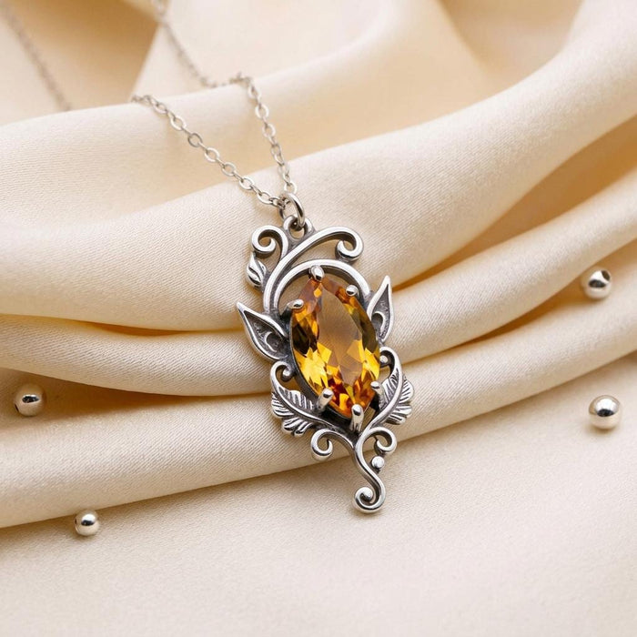 Elven Birthstone Necklace with a marquise-shaped stone, leaf details, feather-like accents, and scrollwork on cream satin