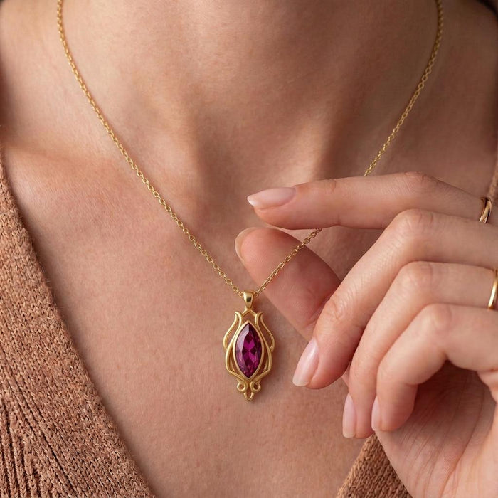 Hand holding a Gold Plated Silver Elven Forest Birthstone Necklace with a magenta marquise-shaped stone