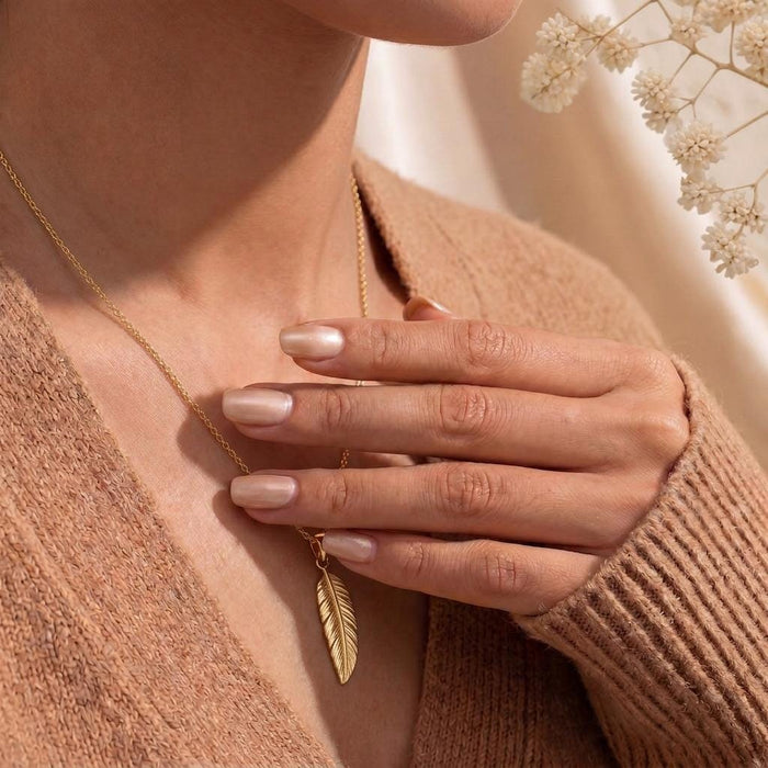 Gold Plated Silver engraved feather pendant necklace held at the neckline over a beige cardigan