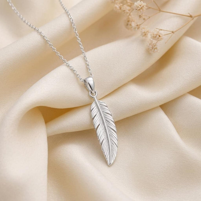 Silver engraved feather pendant necklace arranged on ivory satin with dried flowers