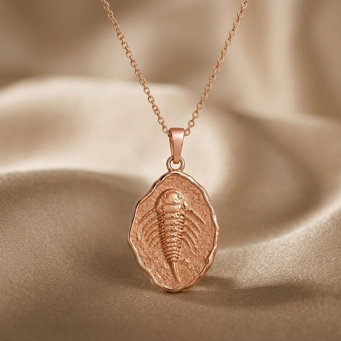 Rose Gold Plated Eurypterid Fossil Pendant Necklace with a textured irregular-edge medallion on beige satin