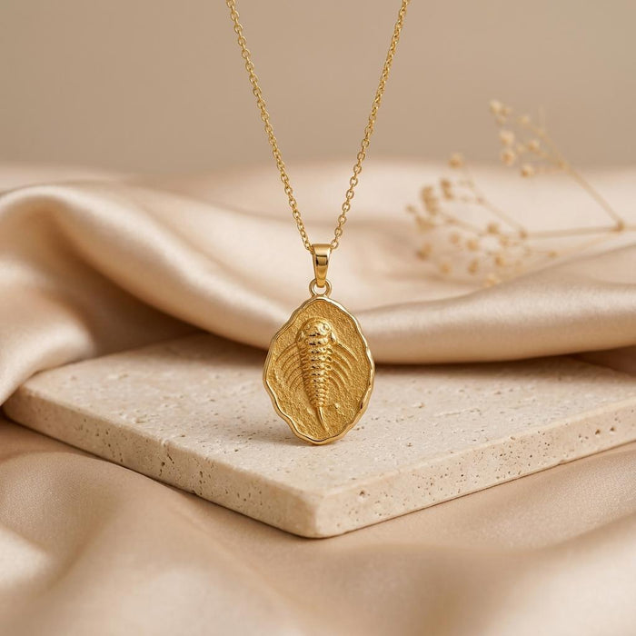 Gold Plated Silver Eurypterid Fossil Pendant Necklace displayed above a light stone block and champagne satin