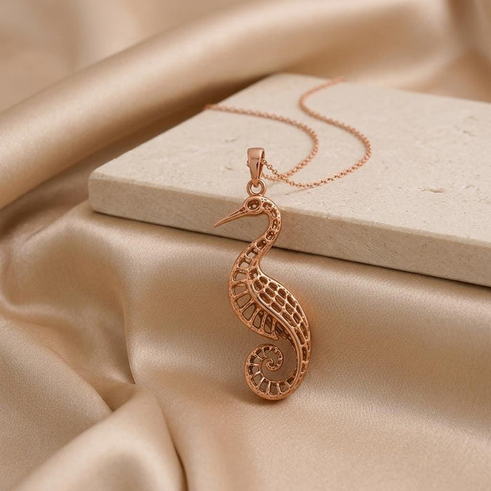 Rose Gold Plated Fossil Crane Pendant Necklace beside a pale stone slab on champagne satin