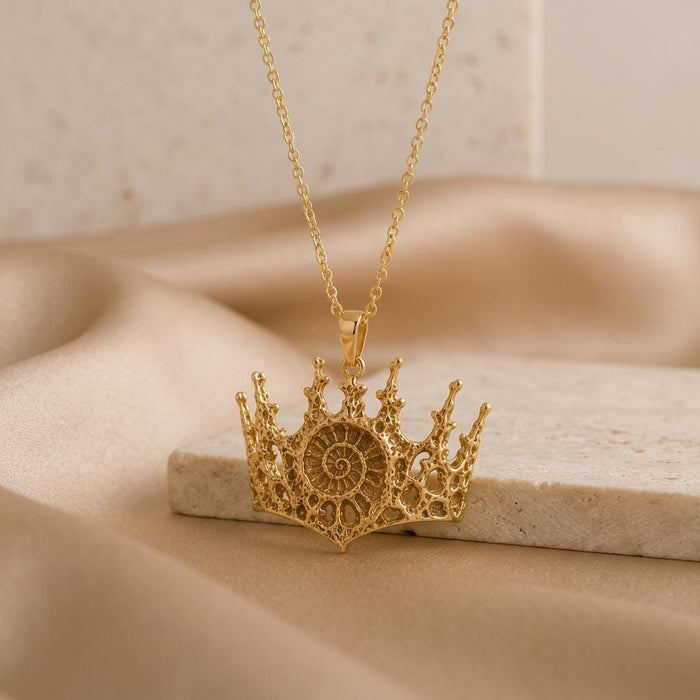 Gold Plated Silver Fossil Crown Necklace with pointed openwork crown pendant displayed on a stone block