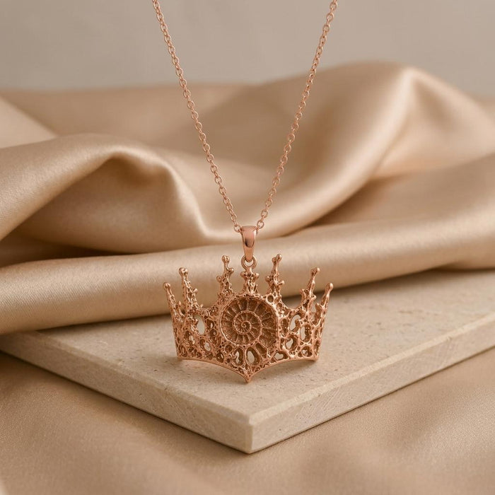 Rose Gold Plated Fossil Crown Necklace with spiral center displayed on a pale stone slab and satin