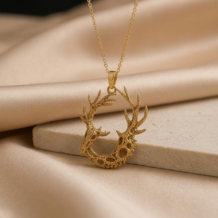 Gold Plated Silver Fossil Deer Relic pendant with openwork antlers displayed on a stone block and beige satin