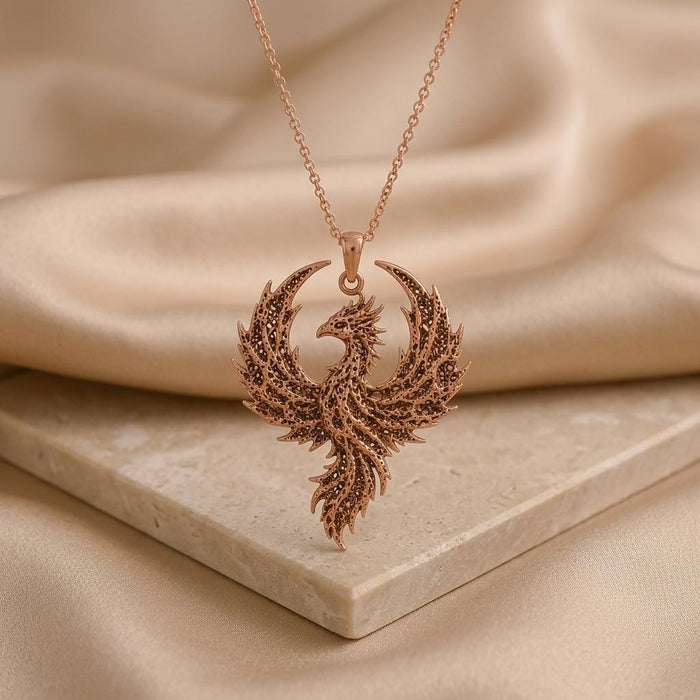 Rose Gold Plated Fossil Phoenix Crest Necklace on a pale stone slab with beige draped fabric