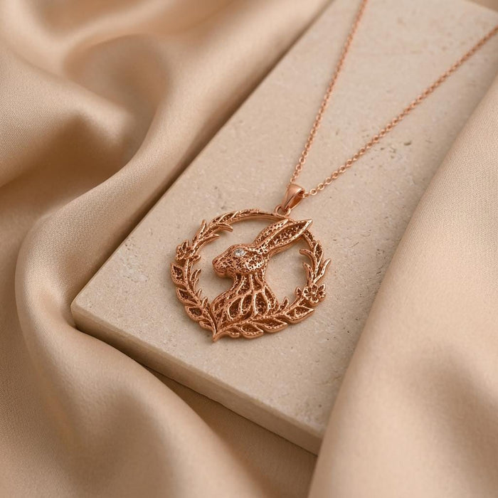 Rose Gold Plated Fossil Rabbit Halo Necklace on a pale stone block surrounded by champagne satin
