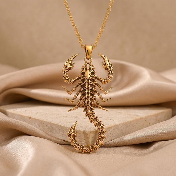 Gold Plated Silver Fossil Scorpion Spine Necklace on cream satin above a rectangular stone block
