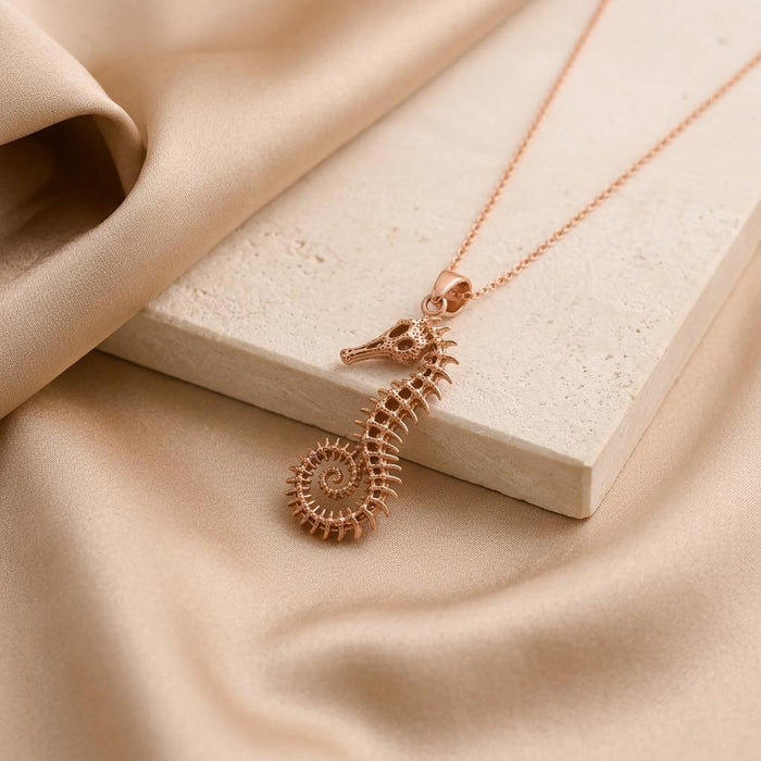 Rose Gold Plated fossil seahorse spine pendant necklace displayed on a pale stone block and champagne satin