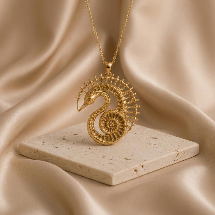 Gold Plated Silver Fossil Swan Halo Pendant Necklace on a stone slab with champagne satin