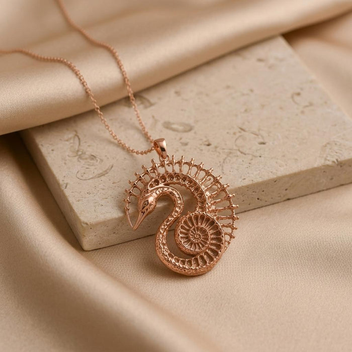 Rose-toned Fossil Swan Halo pendant displayed on a stone slab with champagne satin