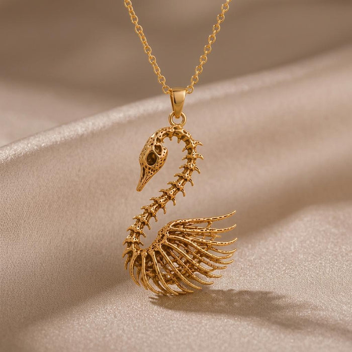 Gold Plated Silver Fossil Swan Skeleton Necklace with curved skull, vertebrae, ribcage, and wing-bone pendant on champagne satin