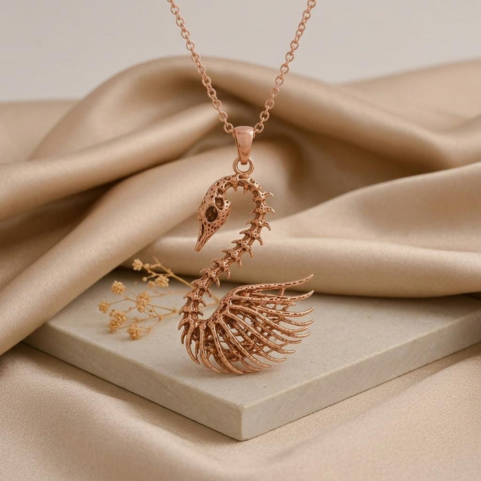 Rose Gold Plated Fossil Swan Skeleton Necklace displayed on a pale stone block with satin fabric