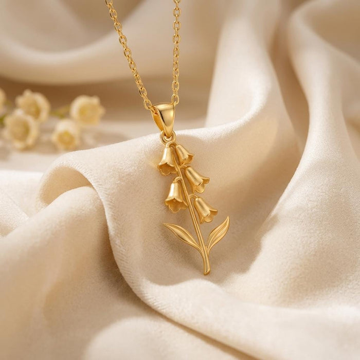 Gold-finish foxglove flower pendant necklace with cascading bell-shaped blooms on cream fabric
