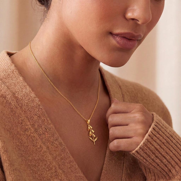 Model wearing a gold-finish foxglove flower pendant necklace with a neutral knit sweater