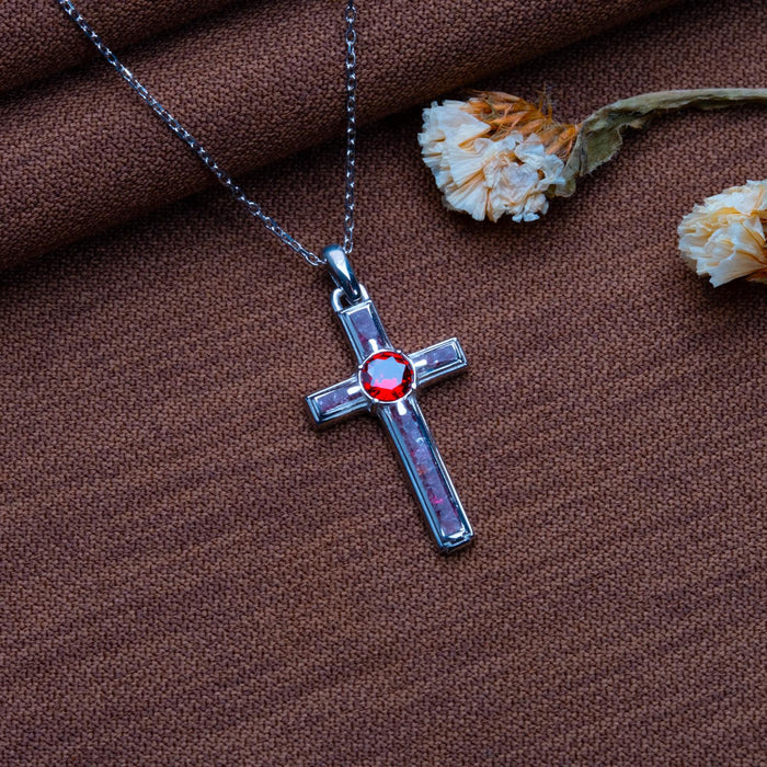 Garnet Birthstone Cross Necklace on brown textured fabric beside dried flowers