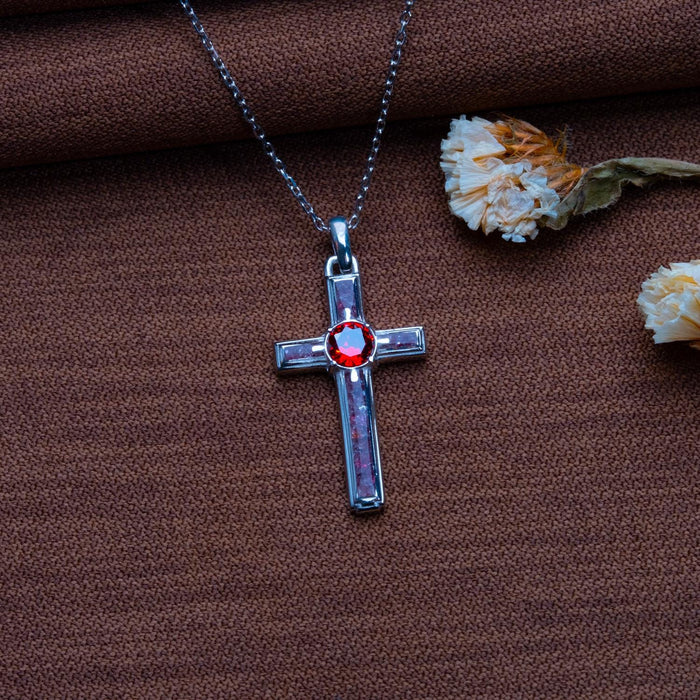 Front view of a Silver Garnet Birthstone Cross Necklace on brown textured fabric