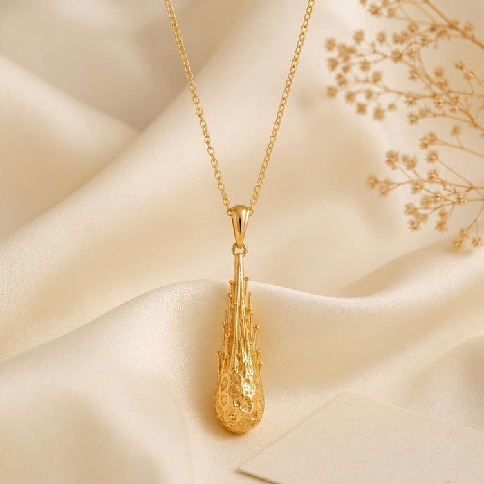 Close view of the Gold Meteor Core Necklace in Gold Plated Silver on ivory fabric beside dried flowers