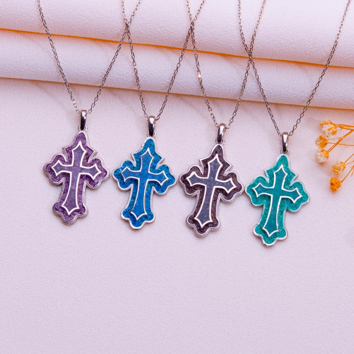 Four scalloped cross pendant necklaces with blue and purple accent inlays arranged on pale pink fabric