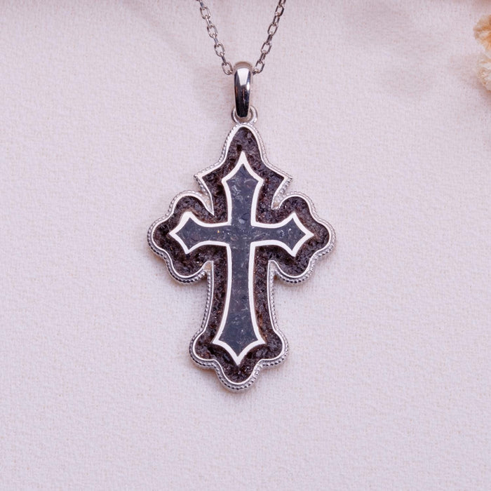Close-up of a dark purple-inlay scalloped cross pendant necklace on pale fabric with dried flowers
