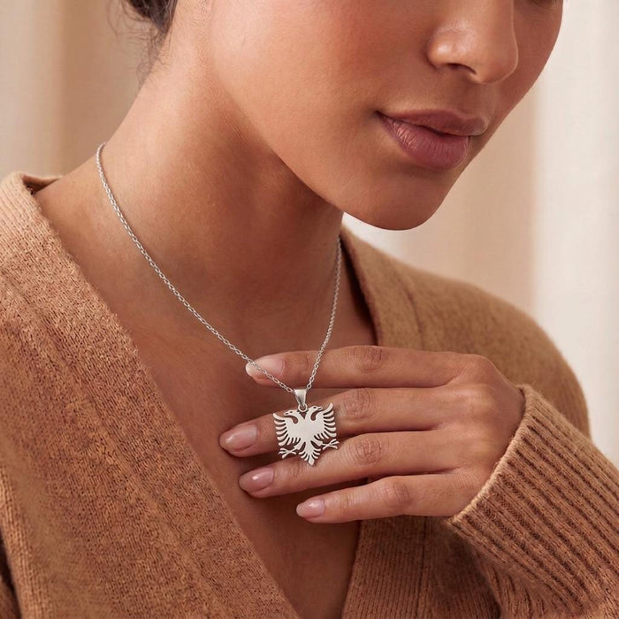 Model holding a silver double headed eagle pendant against a tan knit cardigan