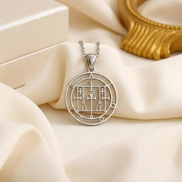 Alloces Seal pendant necklace displayed on ivory satin beside a white jewelry box and gold frame