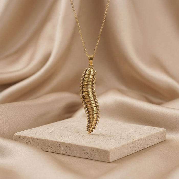 Gold Plated Silver Arthropleura pendant necklace suspended above a light stone display block