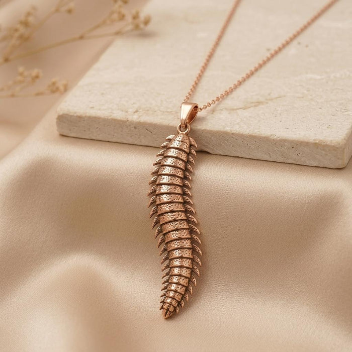 Rose Gold Plated Arthropleura pendant necklace displayed beside a pale stone slab