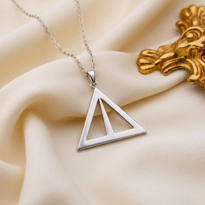Asia Symbol Necklace triangular openwork pendant displayed on ivory satin beside gold decor