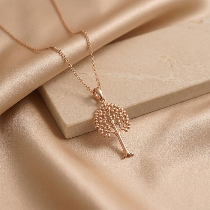Rose-tone Aspen Glow tree pendant necklace displayed on a stone slab over champagne satin