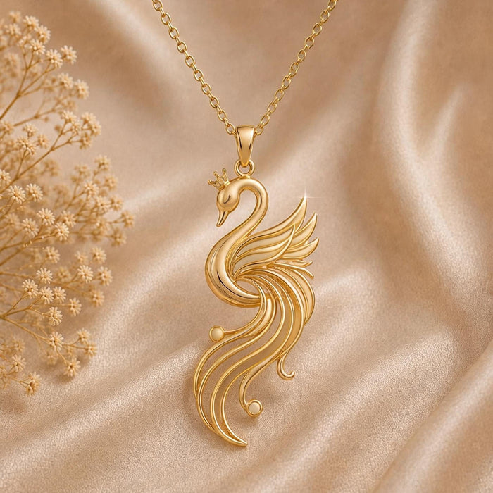 Gold Plated Silver Aurora Swan Pendant with a crowned swan and flowing openwork feathers on champagne satin beside dried flowers