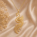 Gold Plated Silver Aurora Swan Pendant with a crowned swan and flowing openwork feathers on champagne satin beside dried flowers