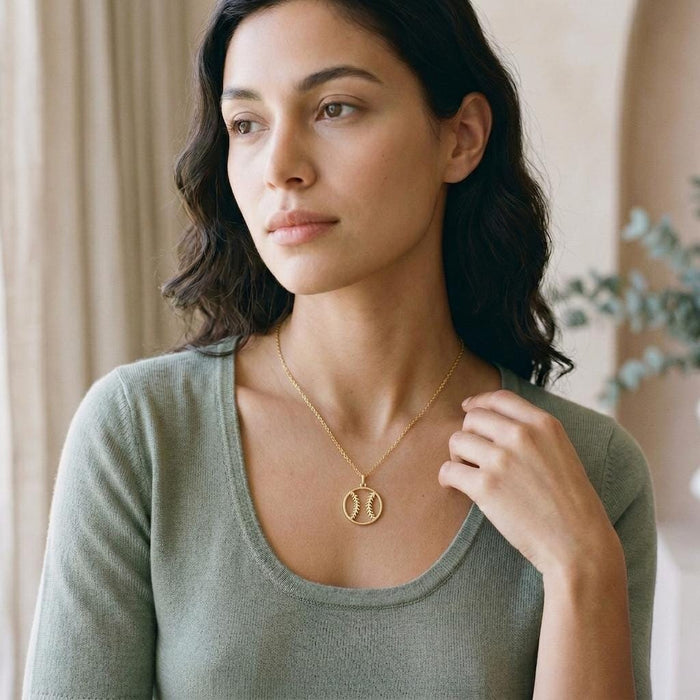 Gold Plated Silver Baseball Necklace with circular seam pendant worn with a soft green scoop-neck top