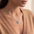 Birthstone Sun Necklace with pointed rays and a round green center stone worn on a V-neck sweater