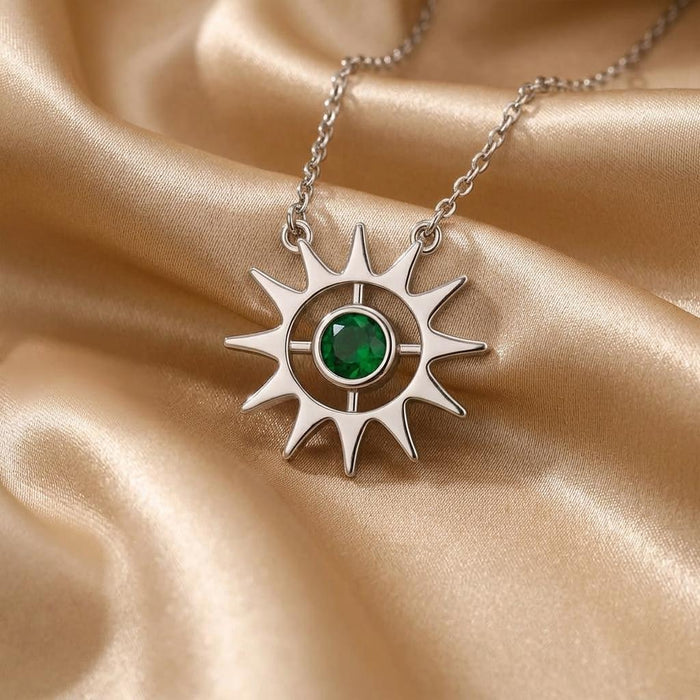 Close-up of the Birthstone Sun Necklace with pointed rays and green center stone on champagne satin