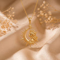 Gold Plated Silver Cosmic Queen Necklace with crowned profile and crescent frame on champagne satin beside dried floral stems