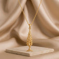 Gold Plated Silver Cypress Flame Pendant hanging above a pale stone slab and beige draped fabric