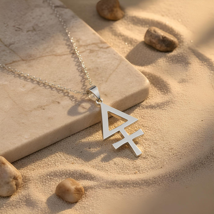 Silver Esoteric Sulfur Necklace with an open triangular symbol pendant on sand beside a stone slab