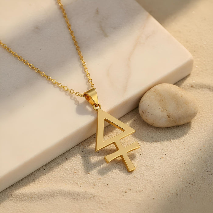 Gold Plated Silver Esoteric Sulfur Necklace with a geometric pendant on sand beside a pale stone slab