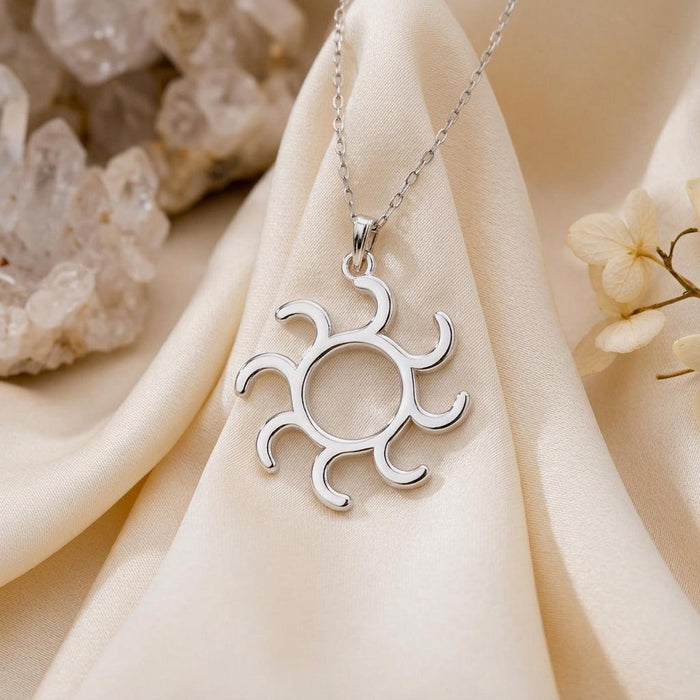 Gold Symbol Necklace pendant with eight curved rays displayed on cream satin beside clear crystals and a flower