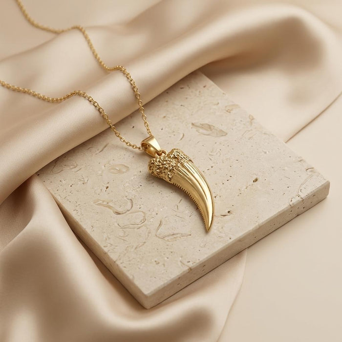 Gold Plated Silver Homotherium fang pendant necklace on a pale stone tile with cream satin
