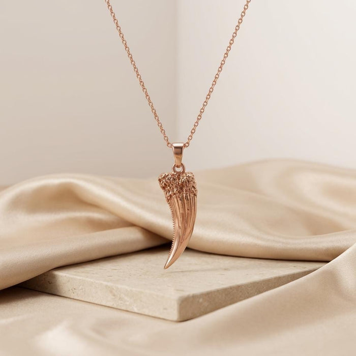 Rose Gold Plated Homotherium fang pendant necklace hanging above a stone display and cream satin