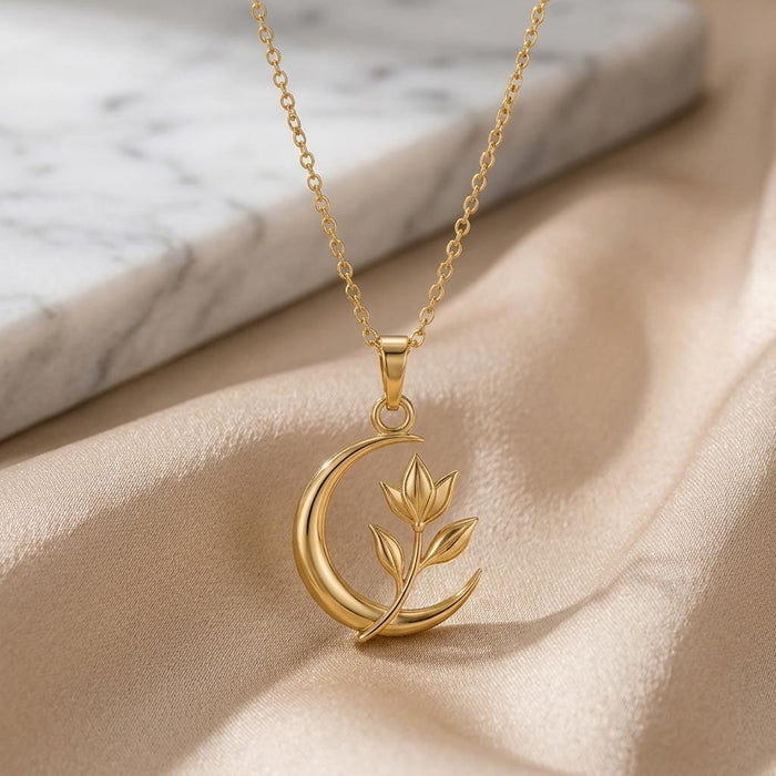 Gold Plated Silver Lunar Petal Pendant with crescent and leaf sprig on champagne satin beside marble