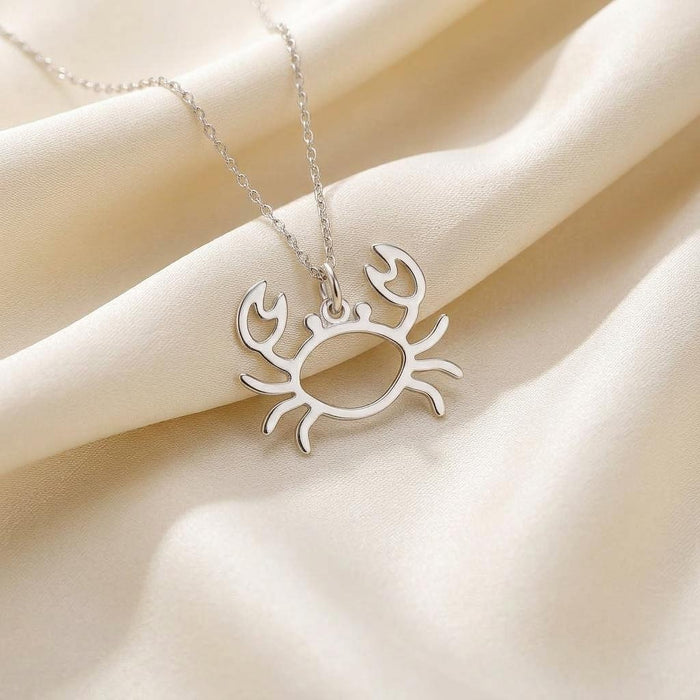 Close-up of a sterling silver openwork crab pendant on cream fabric