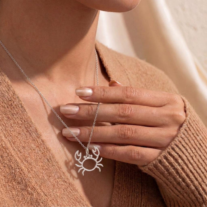 Model holding an openwork crab necklace against a brown knit top